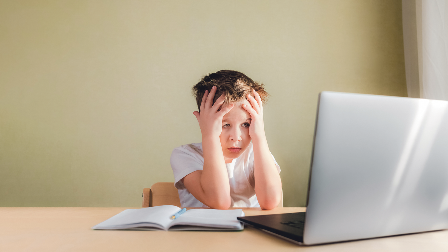 Ein Junge sitzt im Distanzunterricht verzweifelt vor dem Laptop.